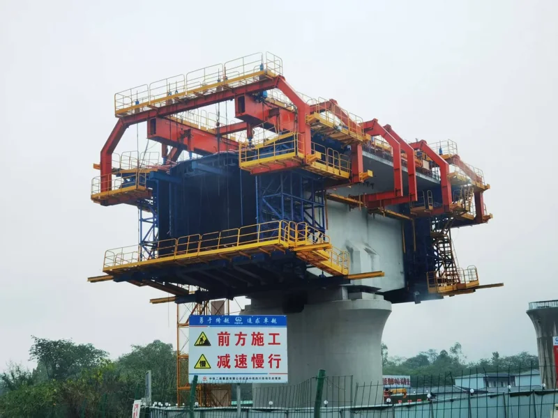 Three-quarter site view of the bridge construction machine around a concrete box-girder segment and pier