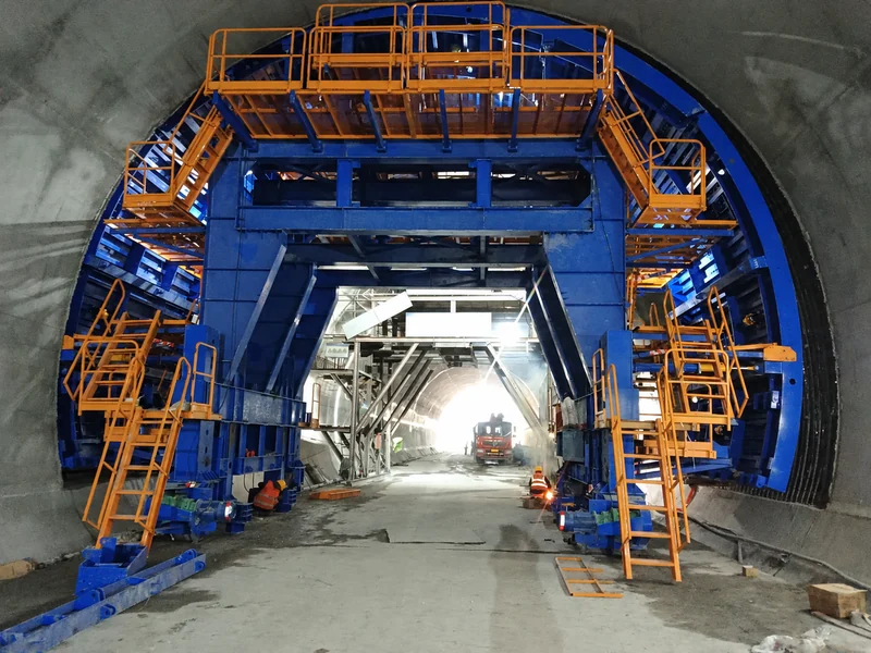 Tunnel lining trolley positioned on side rails inside a tunnel, with access stairs on both sides of the central passage.
